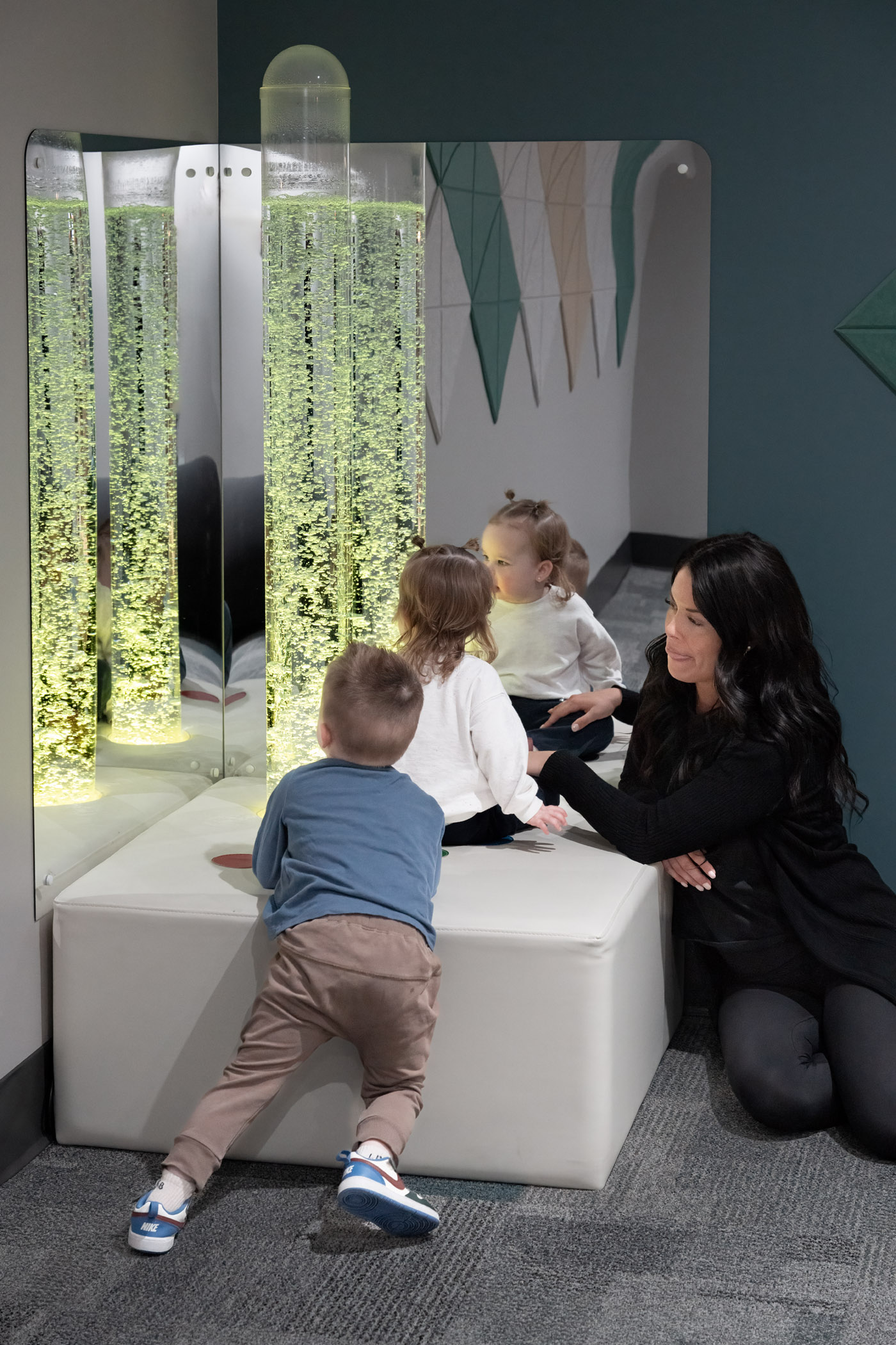 A therapist interacts with children near a bubble wall in a sensory room, offering inclusive event experiences.